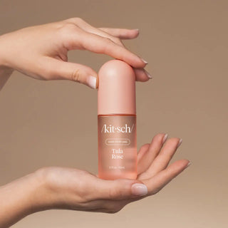 Hand holding a pink bottle of Kitsch Tula Rose perfume against a beige background